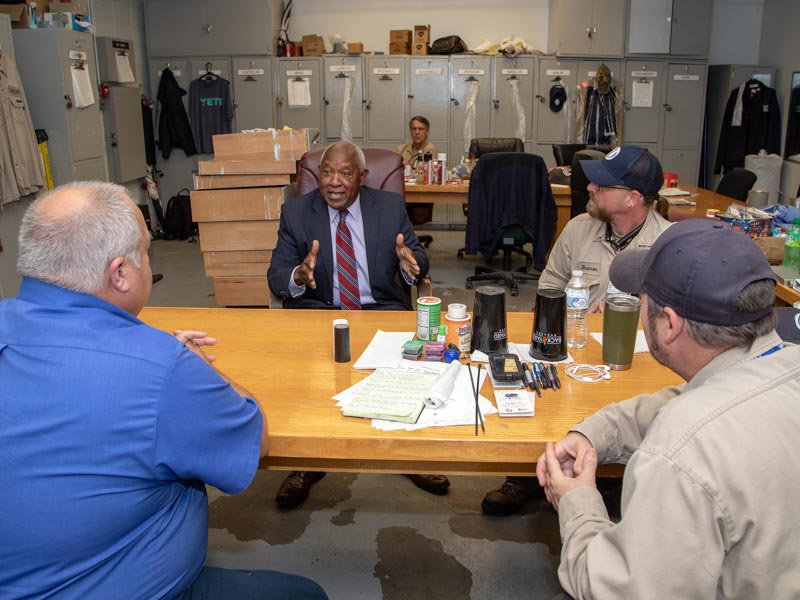 Bogan talks with electrical shop employees Mickey Kilparrick, supervisor (blue shirt), Shannon Eckles, electrician, (ponytail) and James Shaw assistant supervisor